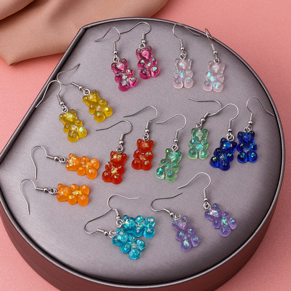 Collection of colorful holographic gummy bear earrings featuring translucent jelly bears in pink, yellow, orange, red, green, blue, purple, and more, all with silver ear hooks, displayed in a round tray