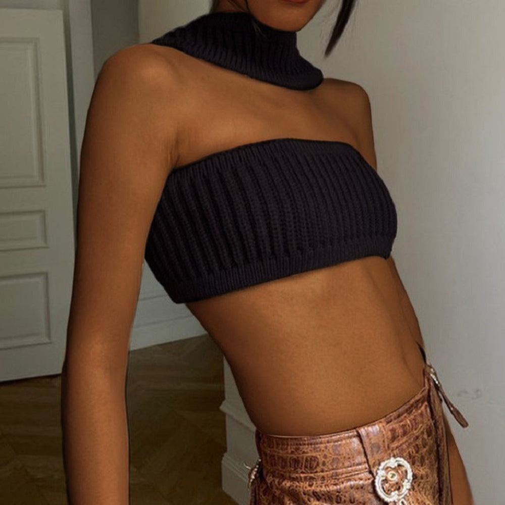 Model wearing a black ribbed knit asymmetrical crop top with high turtleneck collar and strapless bandeau style, paired with brown crocodile-patterned pants with statement buckle.