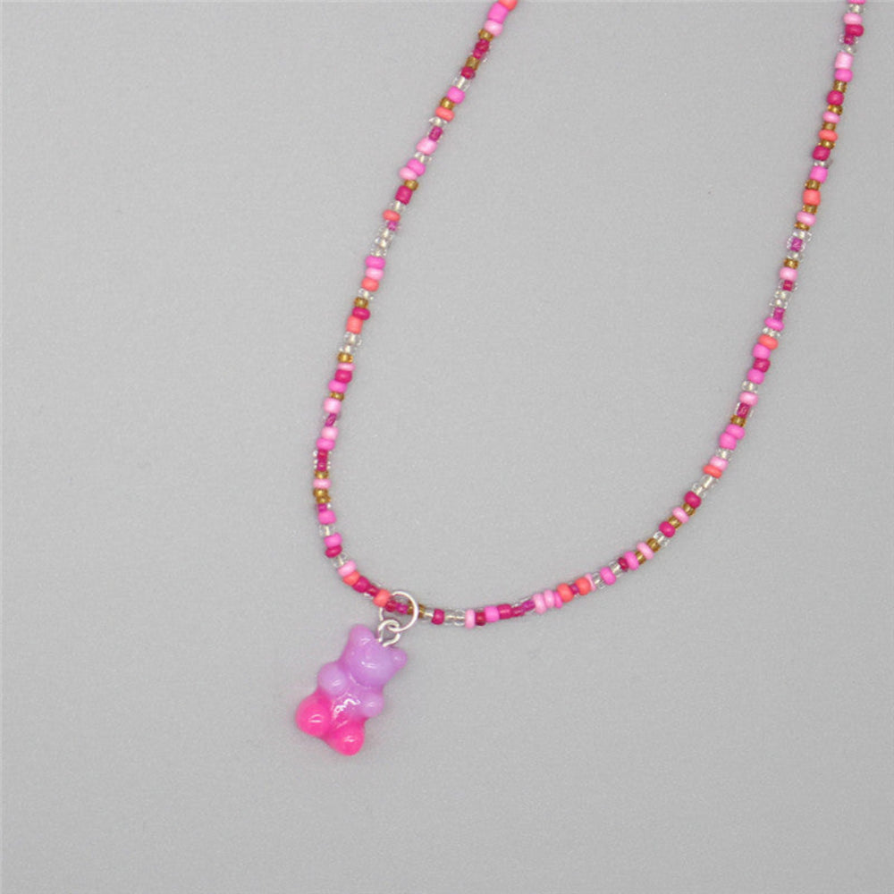 Hot pink beaded necklace with a vibrant mix of magenta, pink, and metallic seed beads paired with a sparkling translucent pink-to-purple ombre gummy bear pendant. Playful single-strand design laid flat on a light gray background, showcasing its bold and feminine style.
