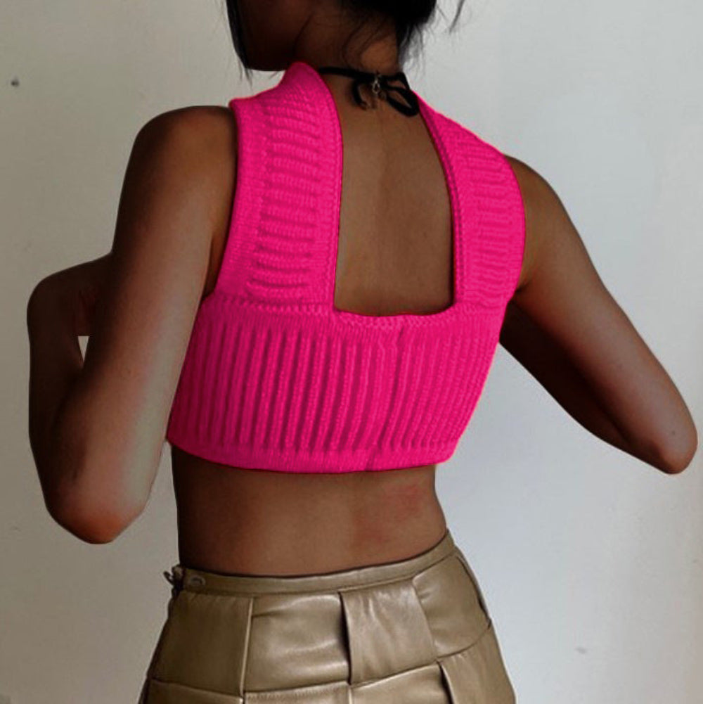 Back view of model wearing a bright pink ribbed knit crop top with high neck, open back design, and sleeveless style, paired with shiny gold pants.