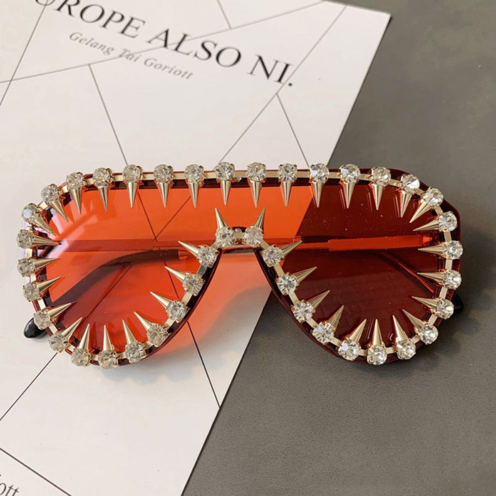 Gold spike crystal sunglasses with orange lenses – trendy designer statement sunnies with spikes and rhinestones, product flat lay.
