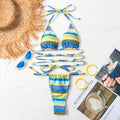 Striped bikini set with sunglasses, hat, and magazine on a textured surface