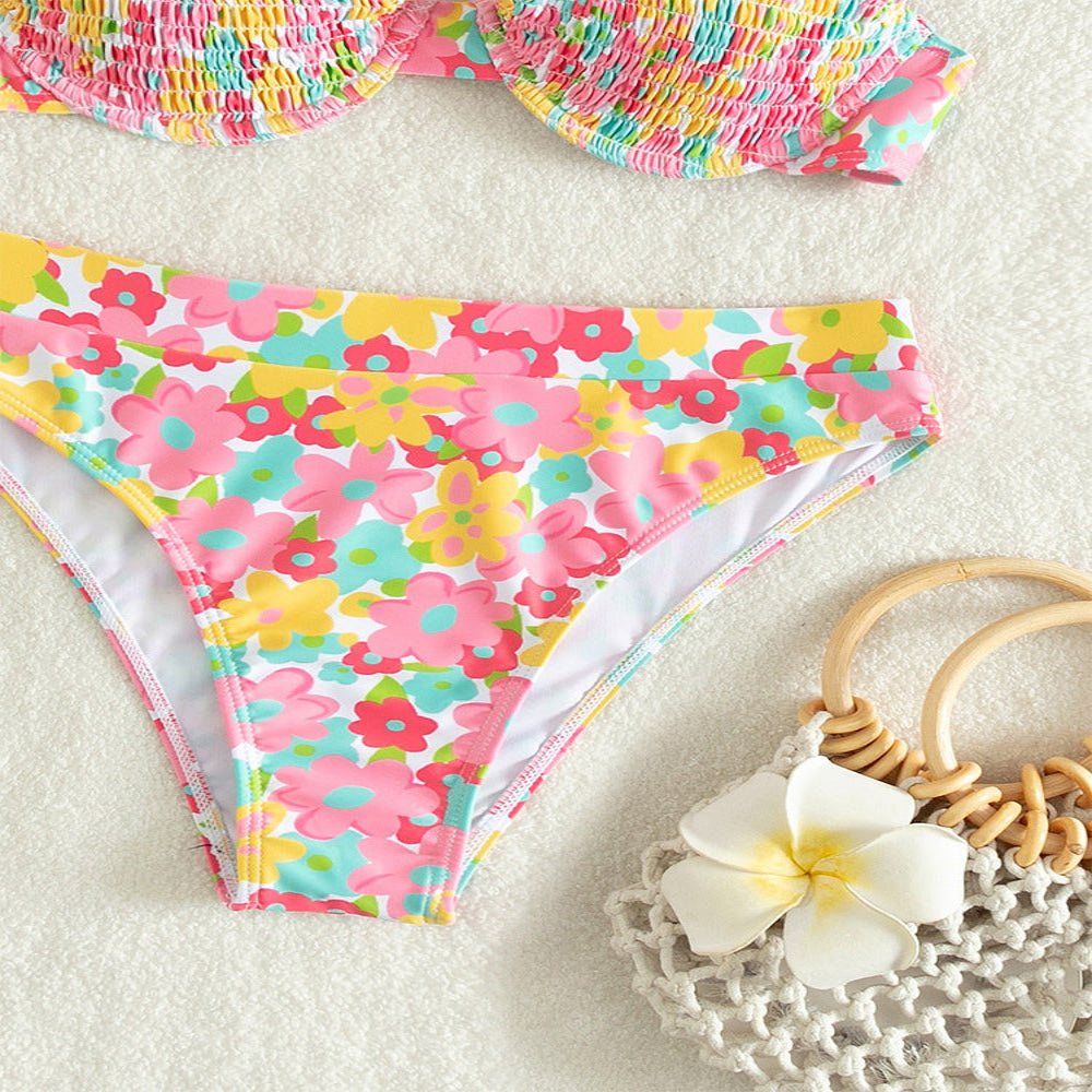 Colorful floral bikini bottom on a textured surface with a white flower and wooden ring.