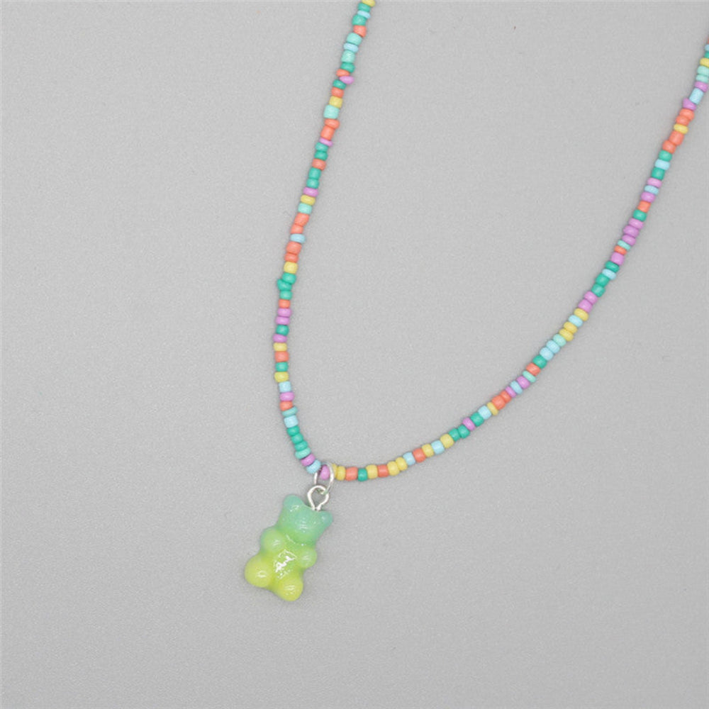 Rainbow pastel beaded necklace featuring a cheerful mix of multicolored seed beads in pink, orange, yellow, green, blue, and purple. It includes a translucent light green gummy bear pendant. The playful single-strand necklace is laid flat on a light gray background, highlighting its fun and vibrant design.