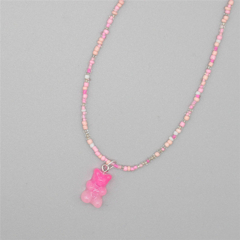 Delicate pink beaded necklace featuring a soft mix of pastel pink, peach, white, and iridescent seed beads with a vibrant bright pink translucent gummy bear pendant. Playful single-strand design laid flat on a light gray background, showcasing its sweet and feminine style