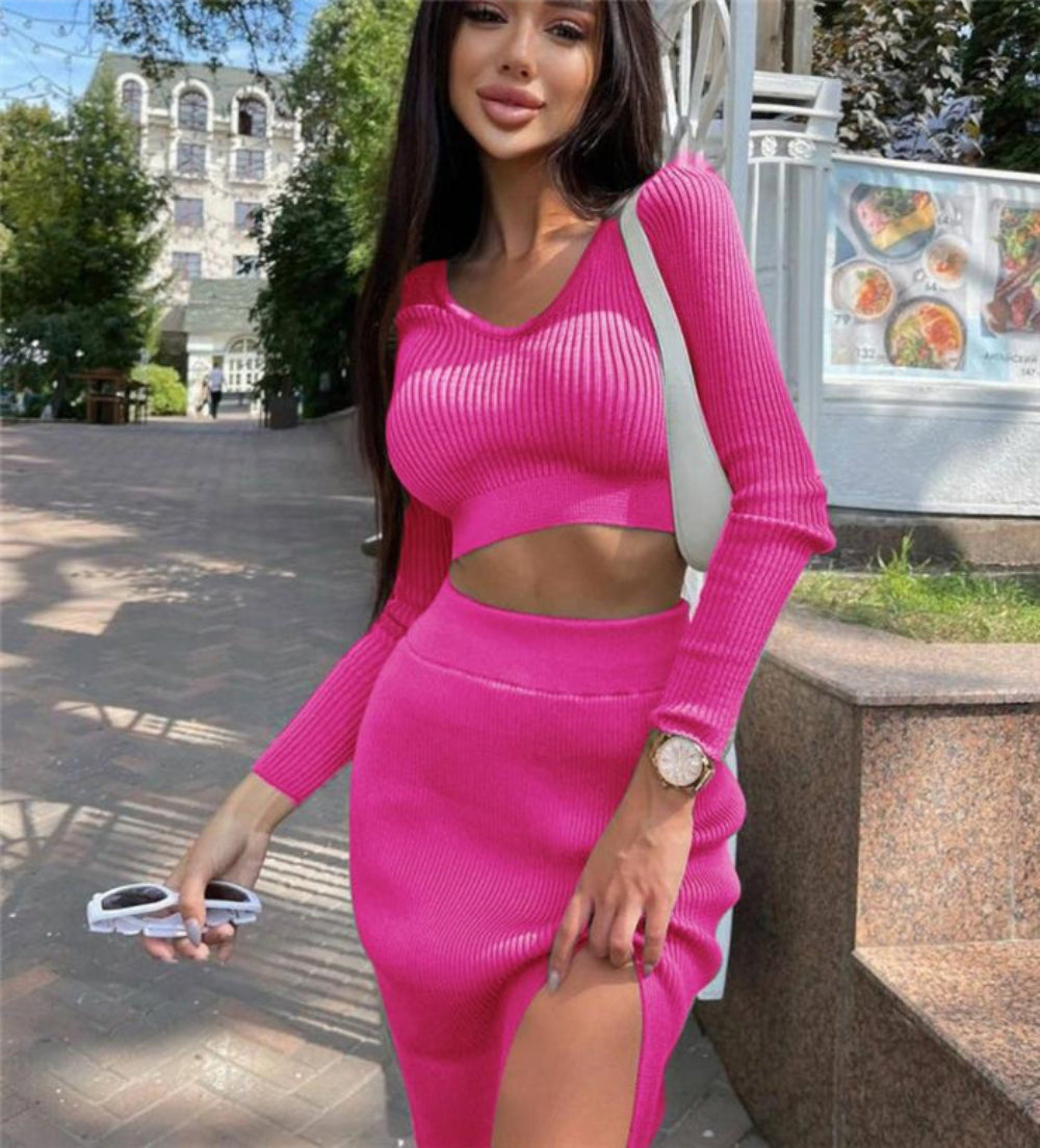 Woman in vibrant pink ribbed long-sleeve crop top and high-slit midi skirt set, standing outdoors on city street.