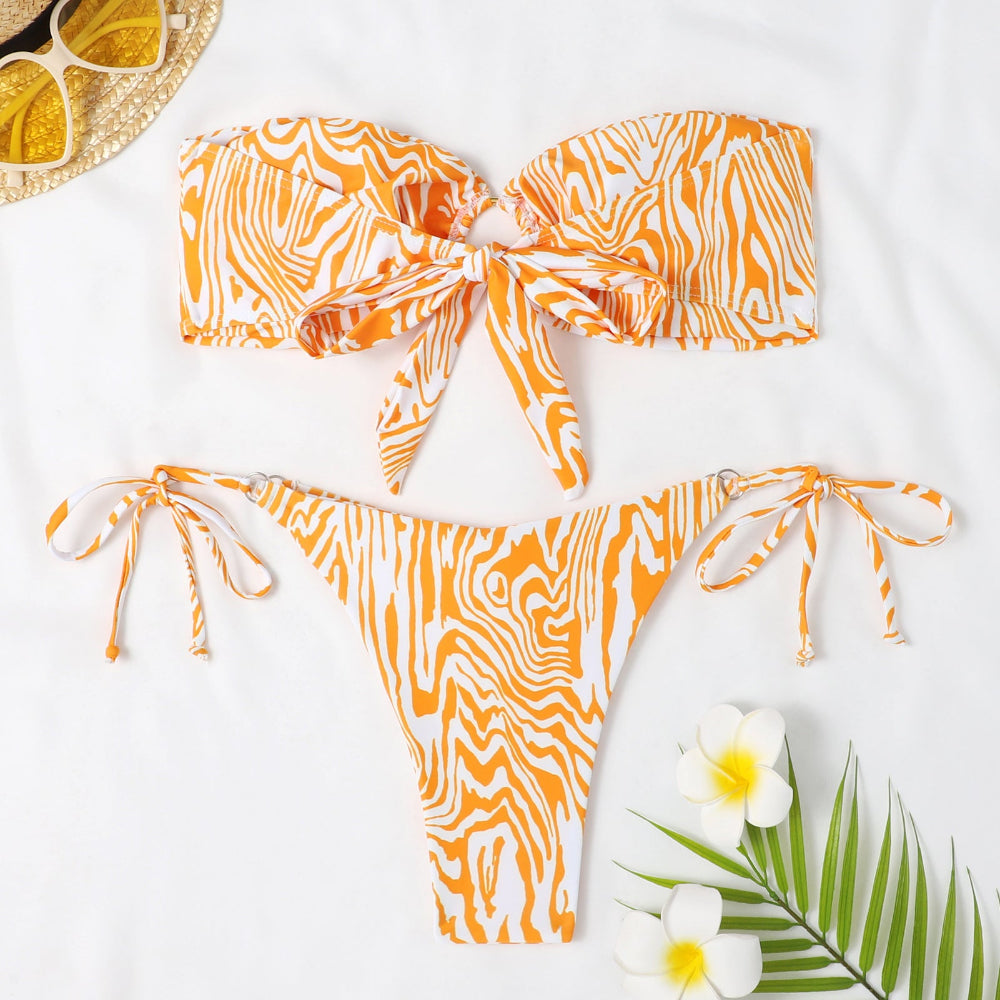 Orange and white patterned bikini set on a white background with sunglasses and flowers.