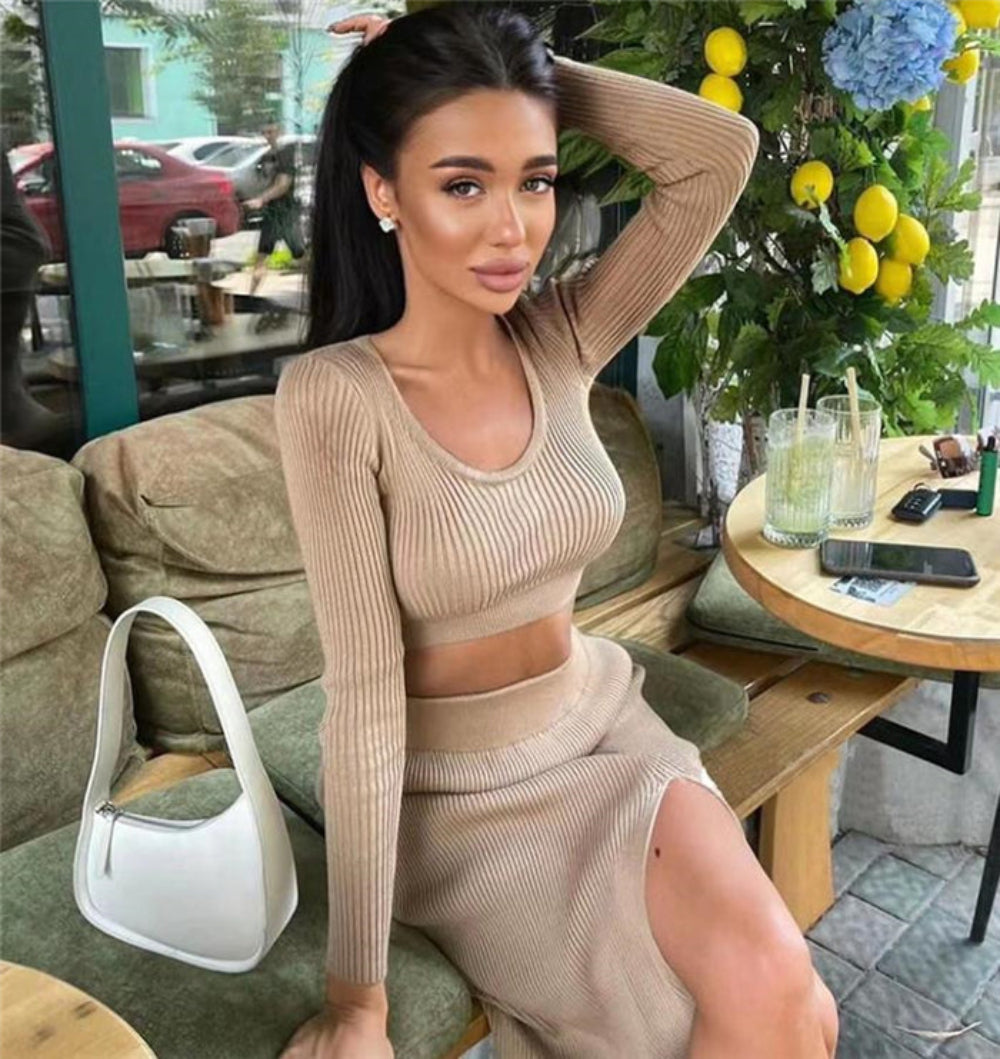 Woman in beige ribbed long-sleeve crop top and high-slit midi skirt set, seated at outdoor cafe with white handbag.